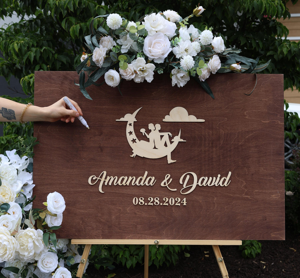 a person writing on a wooden sign with flowers in the background