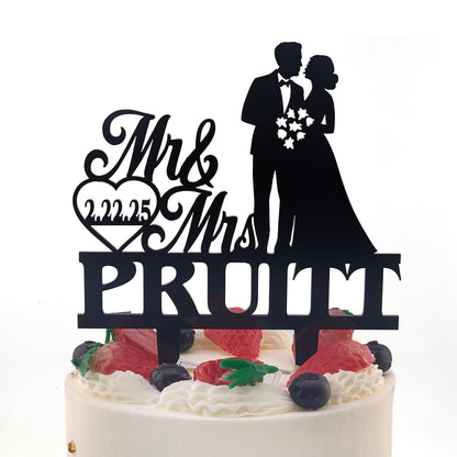 A black silhouette of a bride and groom on a wedding cake topper, with the text "Mr & Mrs PRUITT" and the year "2022.25" displayed below.