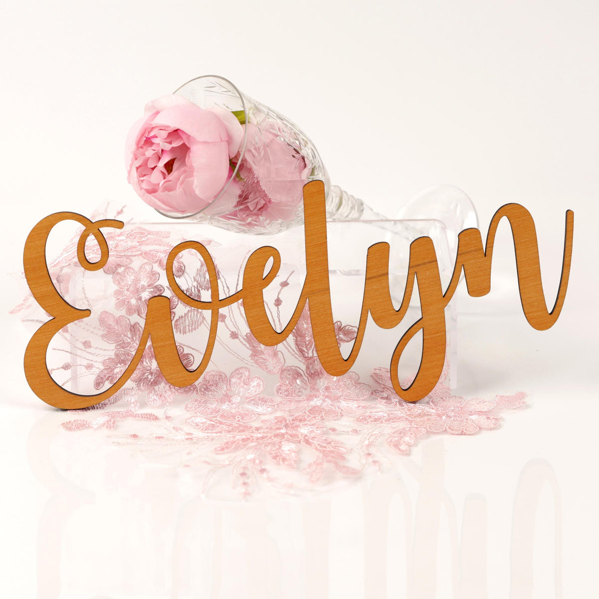 a wooden sign with the name "Evelyn" written on it, along with a glass containing pink flowers and a pink flower petal.