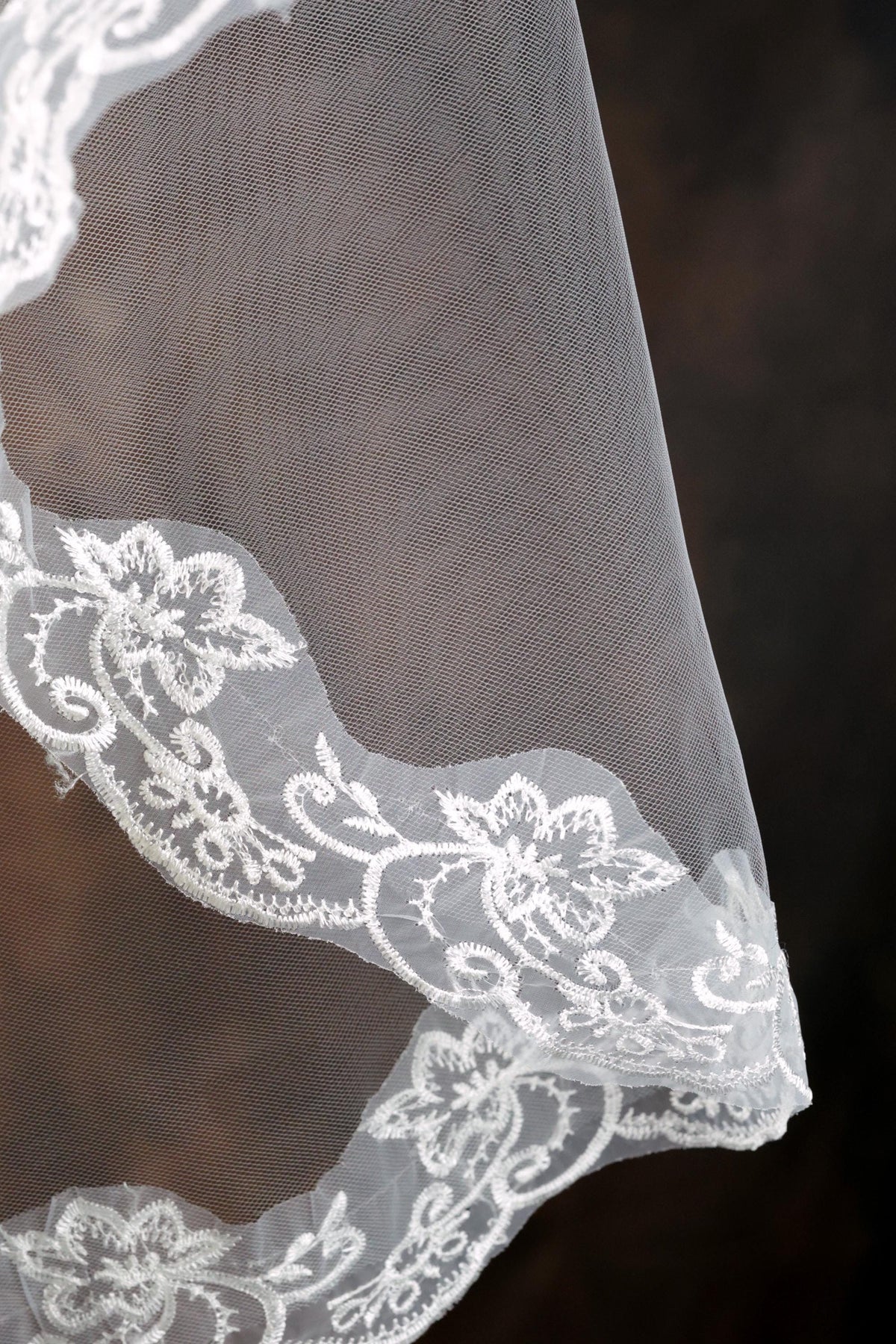 A close-up view of a delicate white lace veil with intricate floral embroidery.