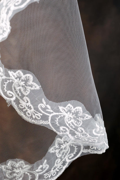 A close-up view of a delicate white lace veil with intricate floral embroidery.