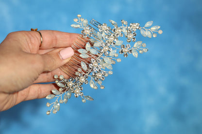 A hand holding a decorative hair accessory with a blue background.