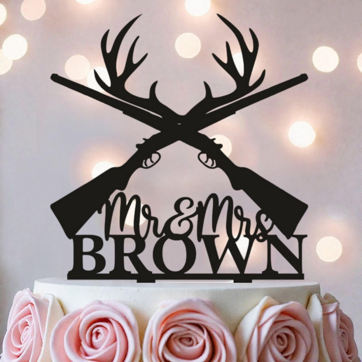 A black silhouette of a crossed rifle with antlers on top of a white cake, with the text "Mr & Mrs Brown" below it.