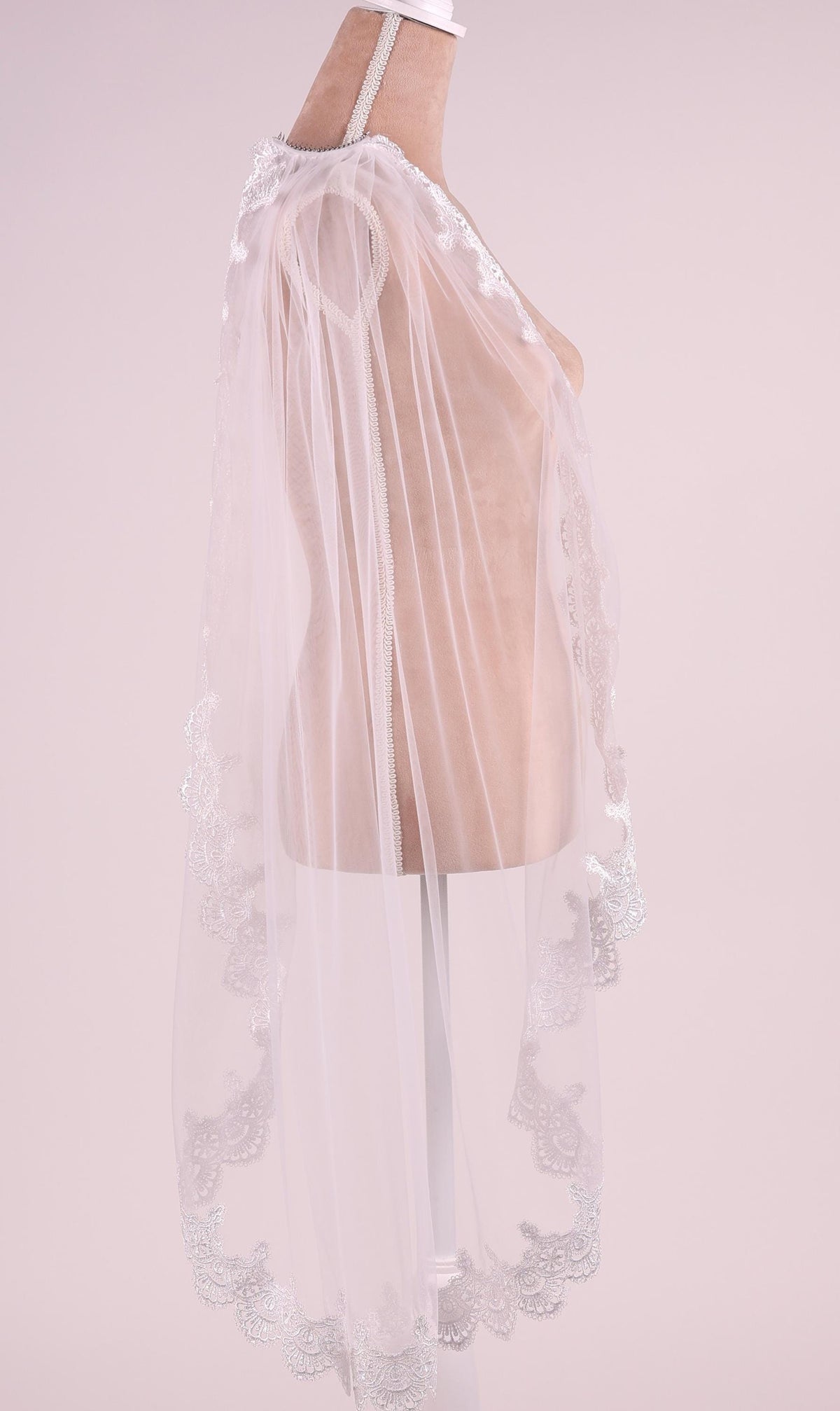 A mannequin wearing a white lace veil with a delicate floral pattern.