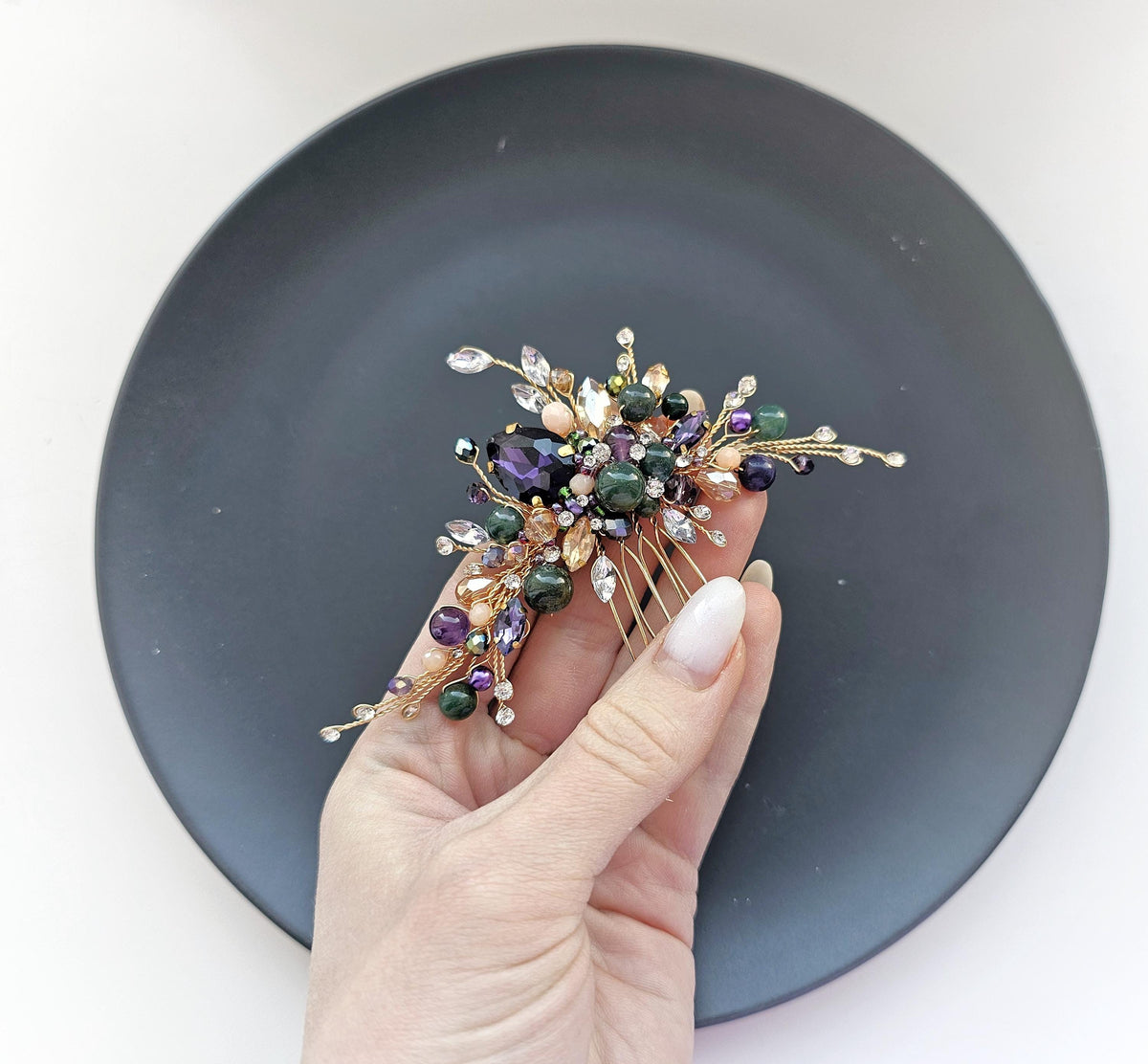 A hand holding a decorative hair accessory with various colorful gemstones and metallic elements.