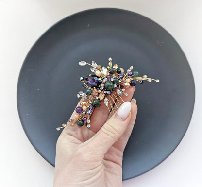 A hand holding a decorative hair accessory with various colorful gemstones and metallic elements.