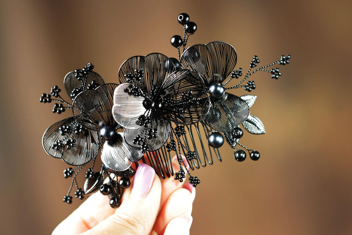 A hand holding a decorative hair accessory with black metal flowers and berries.