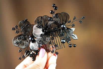 A hand holding a decorative hair accessory with black metal flowers and berries.