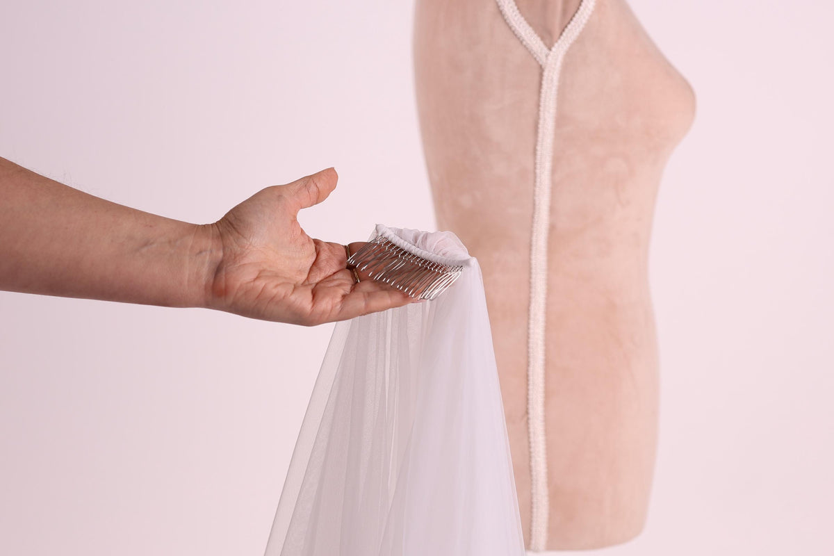 A hand holding a silver hair clip against a white background, with a white dress form visible in the background.