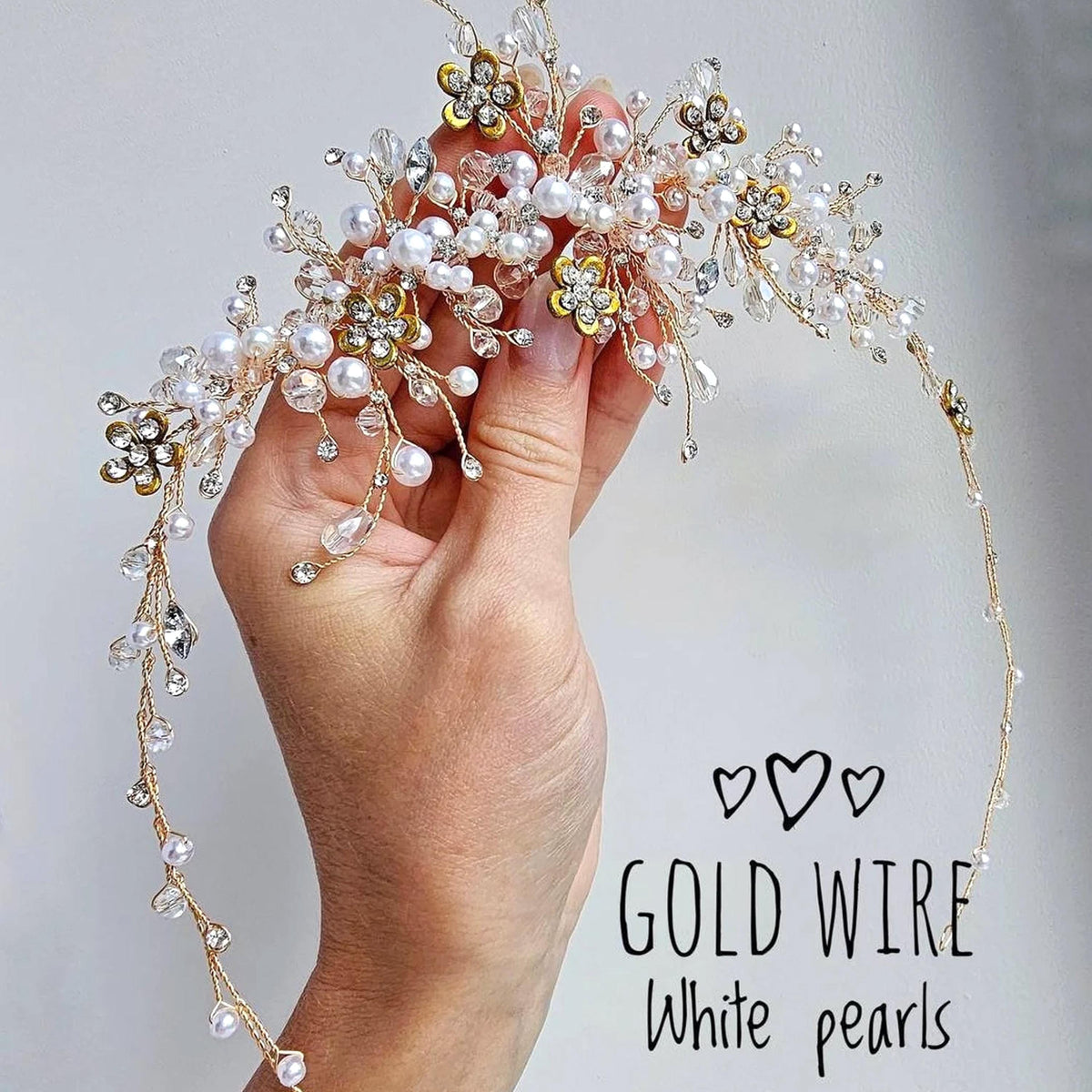 A hand holding a decorative piece of jewelry, which appears to be a combination of gold wire and white pearls.