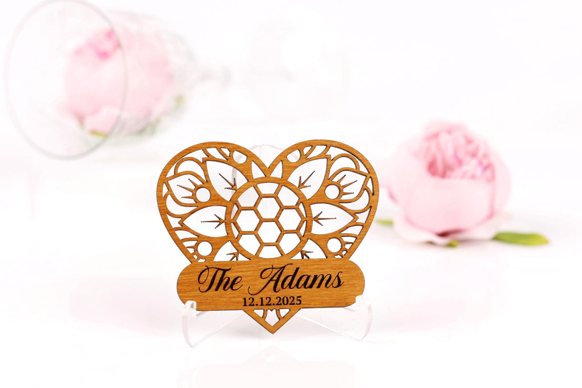A wooden heart-shaped sign with the text "The Adams" and the date "12.12.2025" is displayed in the foreground, with a blurred pink rose in the background.