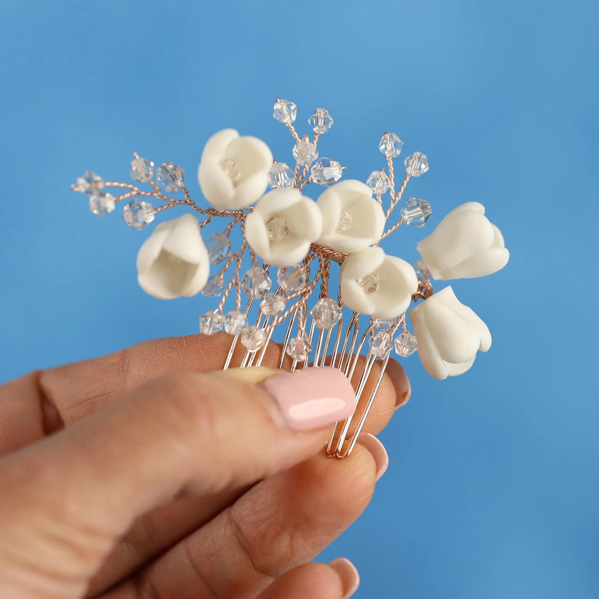 A hand holding a decorative hair clip with white flower-shaped elements against a blue background.
