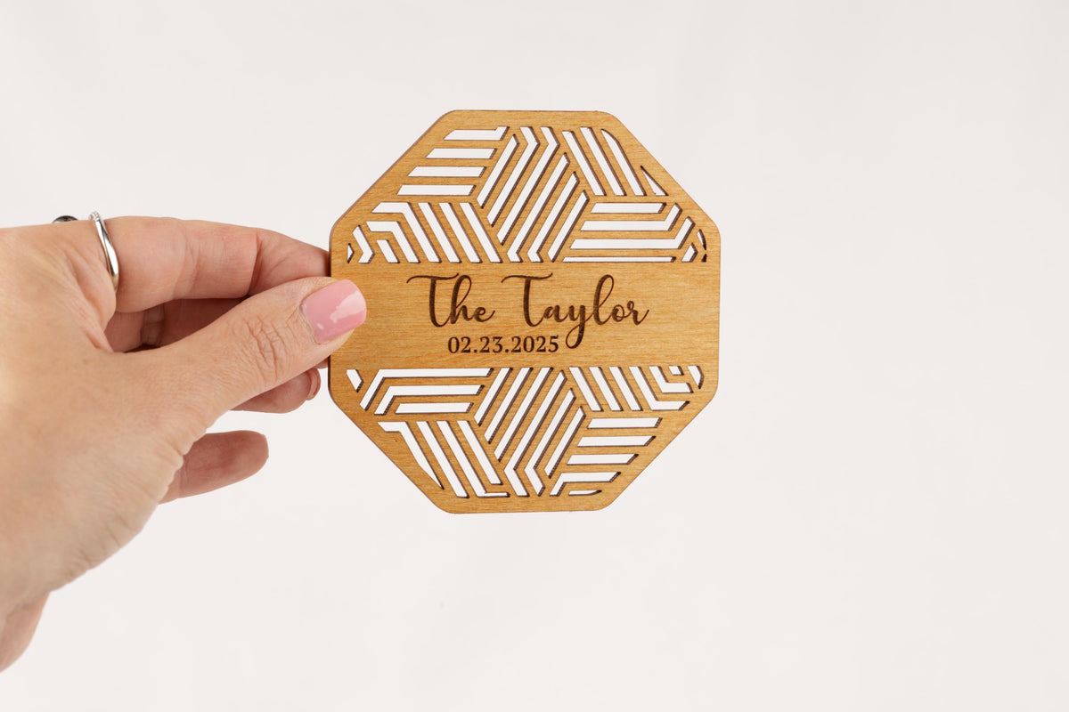 A hand holding a wooden coaster with a geometric pattern and text on it.