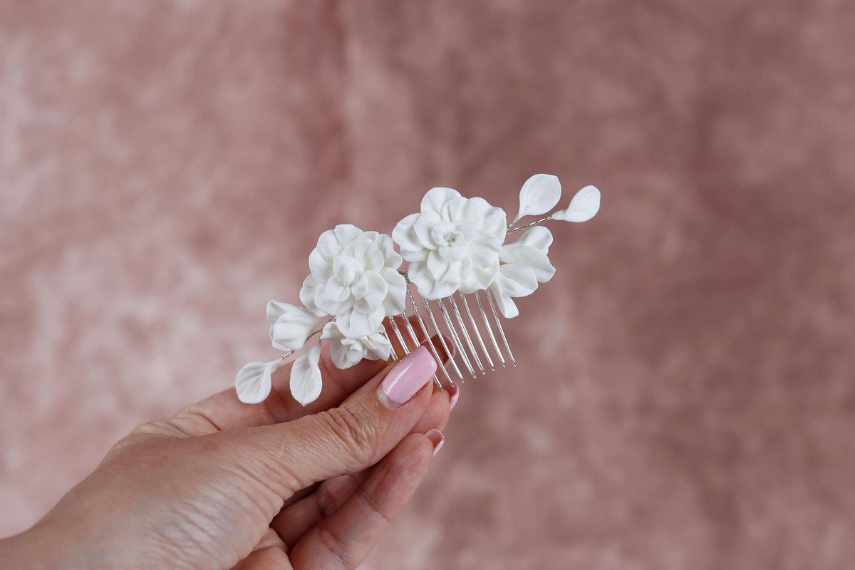 A hand holding a white flower hair accessory against a pink background.
