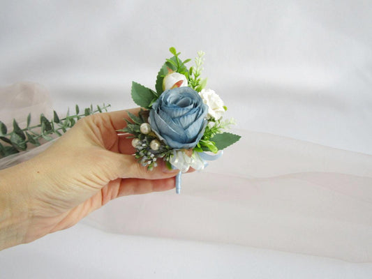 a hand holding a blue and white boutonniere