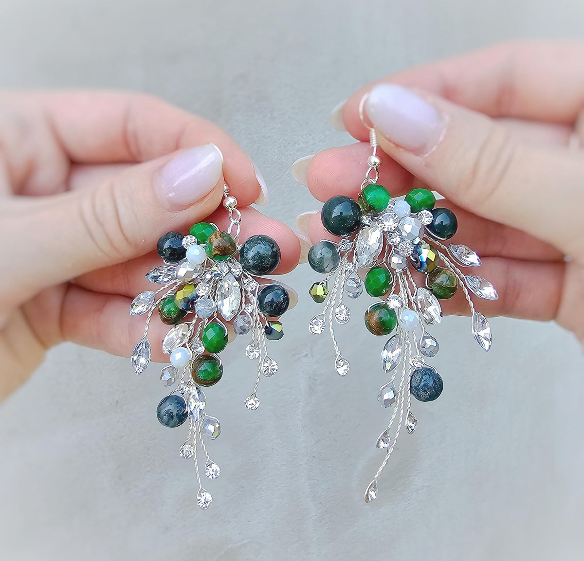 a pair of hands holding a pair of green and white earrings