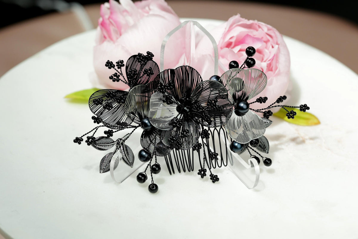 A decorative hair accessory with black and white floral elements, including a black comb and black beads, is displayed on a white surface.