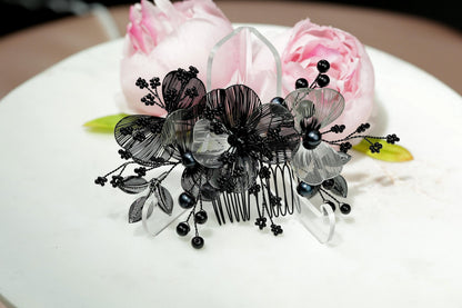 A decorative hair accessory with black and white floral elements, including a black comb and black beads, is displayed on a white surface.