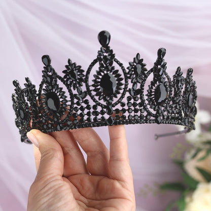 a hand holding a black tiara next to a bouquet of flowers