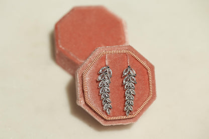 A pair of silver earrings with leaf-shaped designs, displayed in a pink velvet jewelry box.