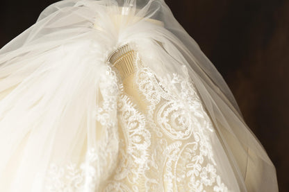 A close-up view of a white wedding dress with a delicate lace veil and a metallic brooch on the back.
