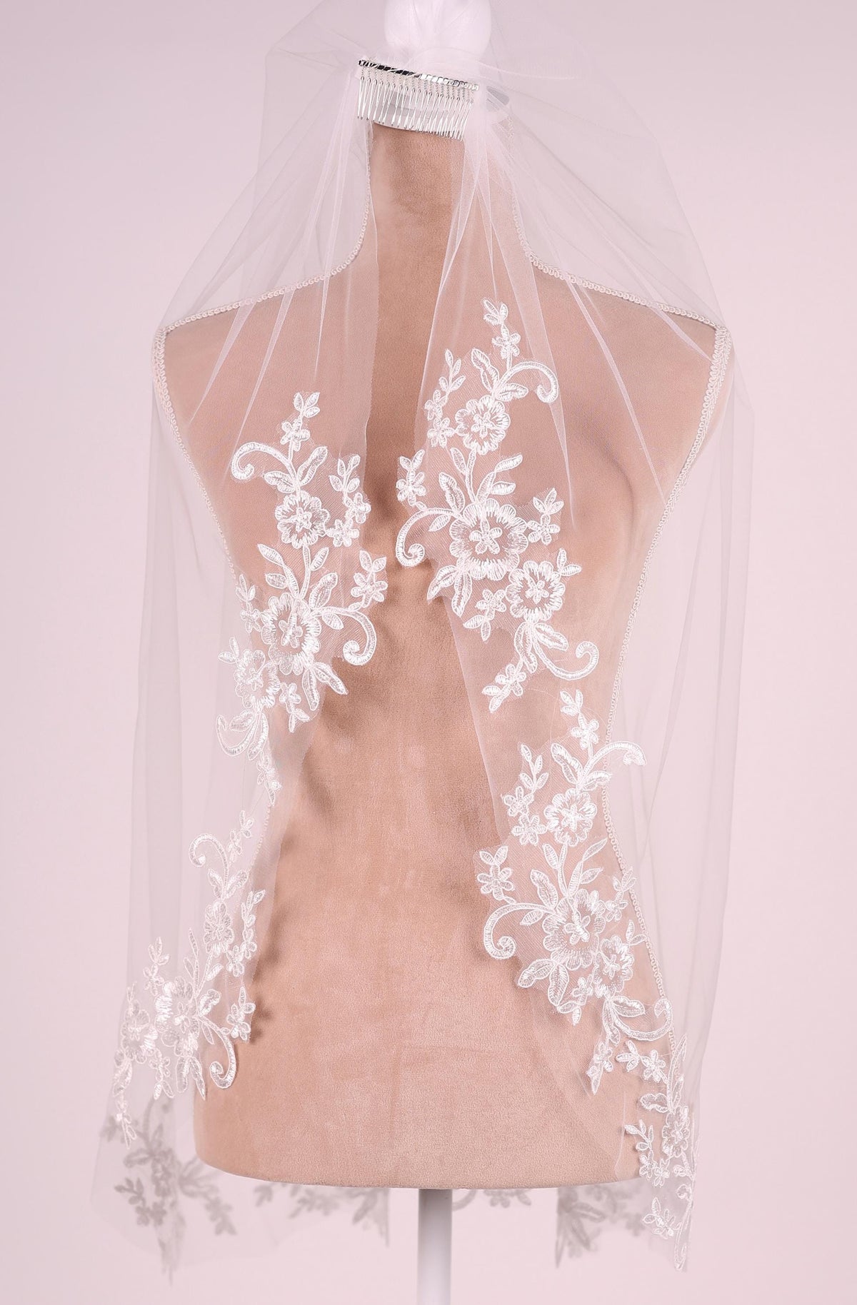 A mannequin wearing a white lace veil with intricate floral embroidery.