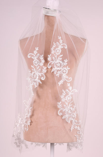 A mannequin wearing a white lace veil with intricate floral embroidery.