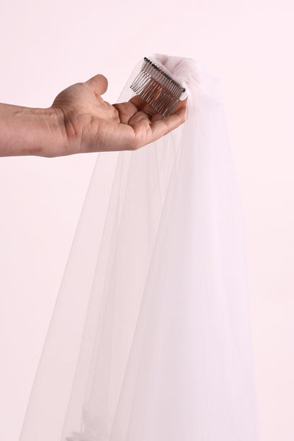 A hand holding a silver hairbrush with a white veil attached to it.