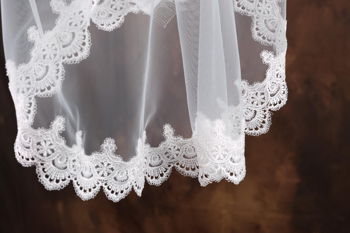 A close-up view of a delicate white lace veil with intricate lace patterns, hanging against a dark background.
