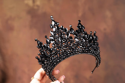 a hand holding a black tiara in front of a brown background
