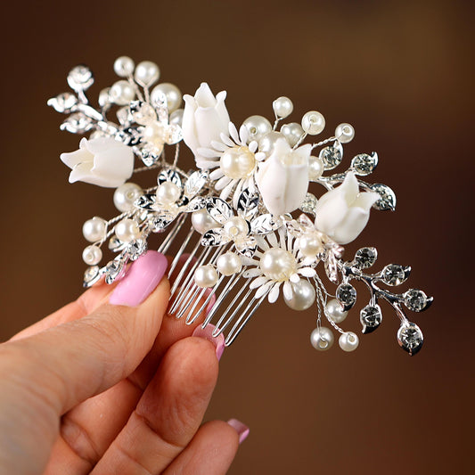 A hand holding a decorative hair clip with white flowers and pearls.