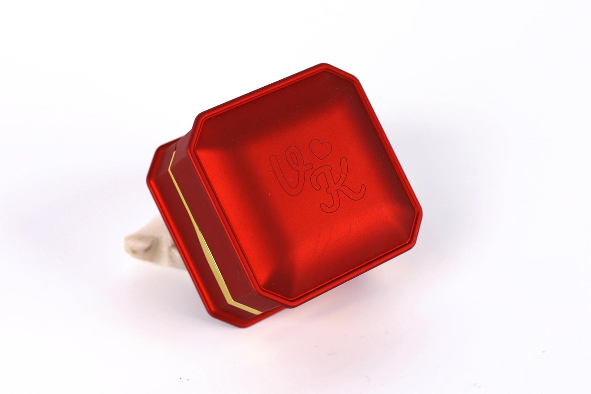 A red metal box with a gold border, featuring a logo or text on its surface.