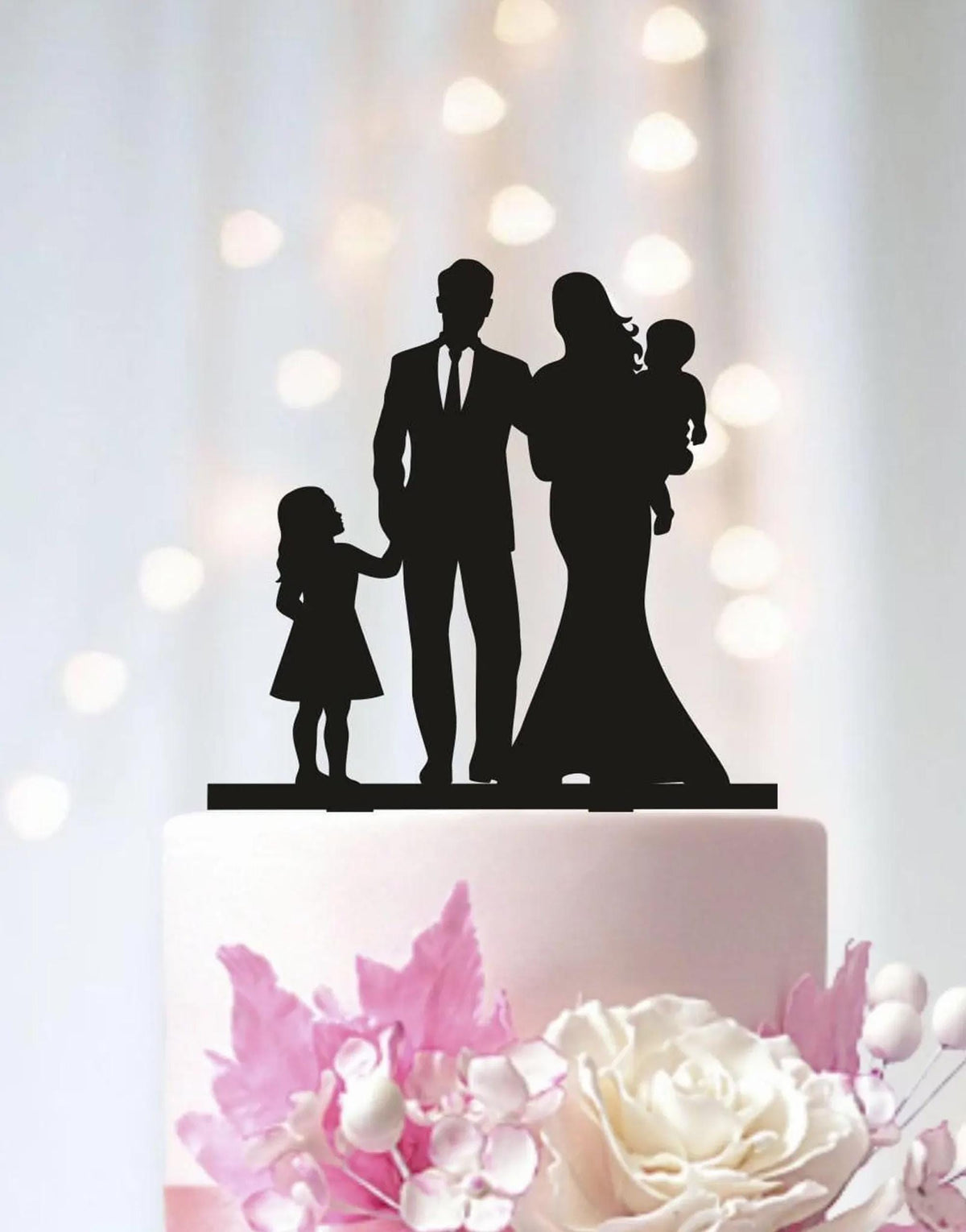 A silhouette of a family, including a man, a woman, and a child, is displayed on top of a white wedding cake.