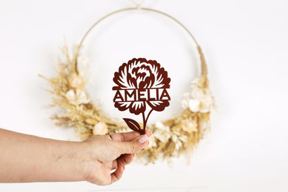 A hand holding a brown paper cutout of a flower with the name "Amelia" written on it.