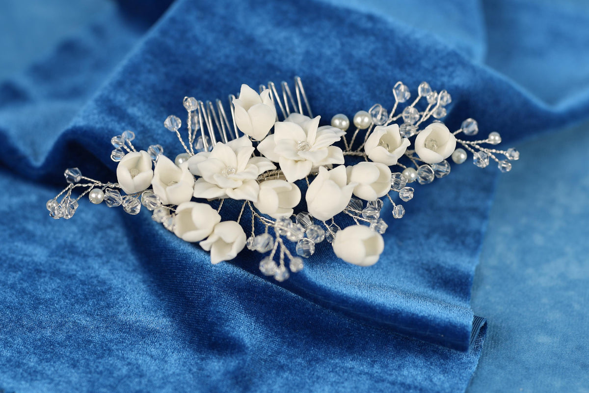 A close-up view of a decorative hair accessory, possibly a hair clip or headband, adorned with white flowers and clear beads, resting on a blue fabric background.
