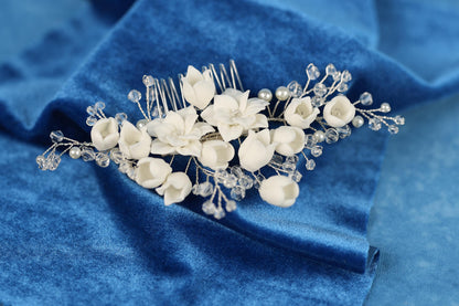 A close-up view of a decorative hair accessory, possibly a hair clip or headband, adorned with white flowers and clear beads, resting on a blue fabric background.