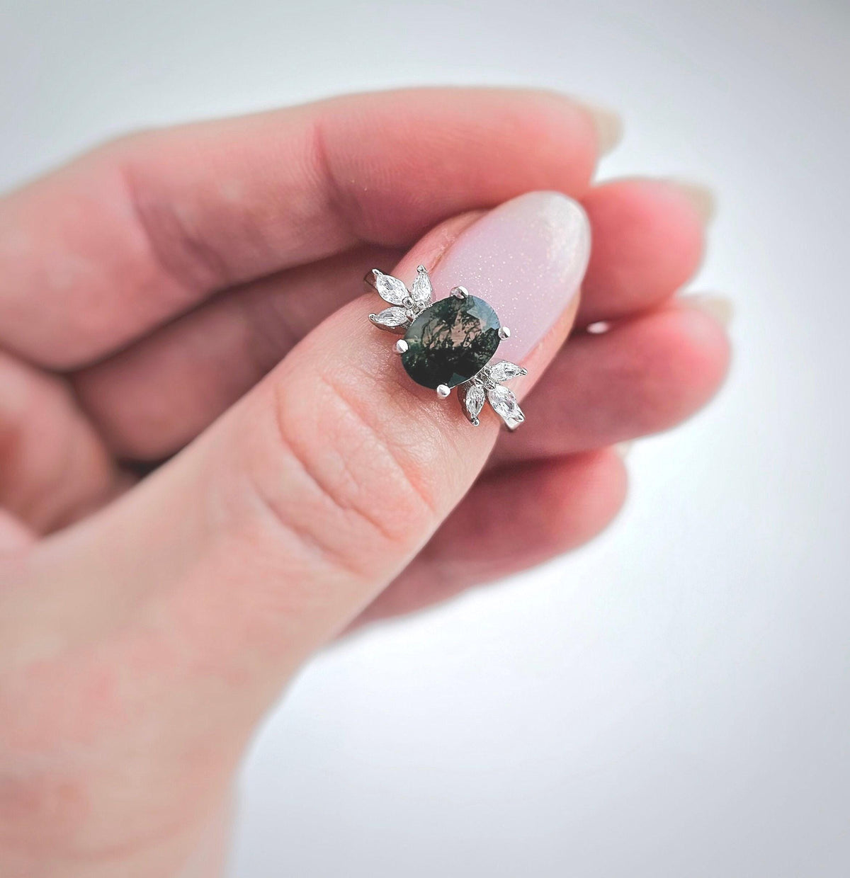 a woman's hand holding a ring with a green stone