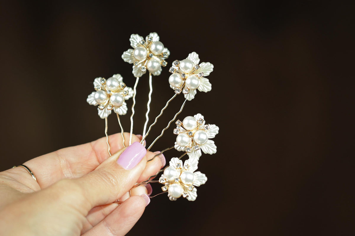 A hand holding a group of white pearl-like flowers with gold accents, against a dark background.