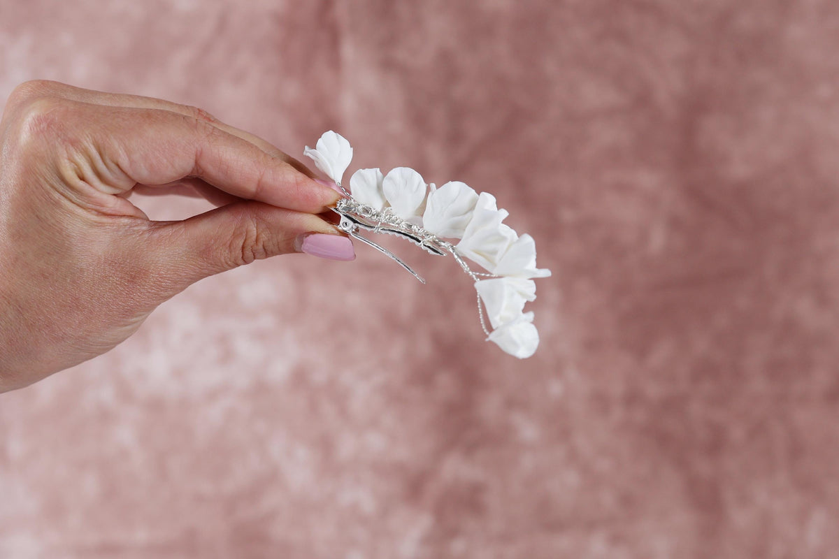 A hand holding a delicate white flower arrangement against a pink background.