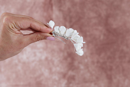 A hand holding a delicate white flower arrangement against a pink background.