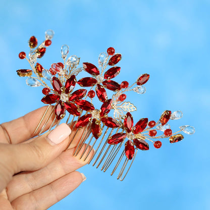 A hand holding a decorative hair accessory with red and gold flowers and gemstones against a blue background.