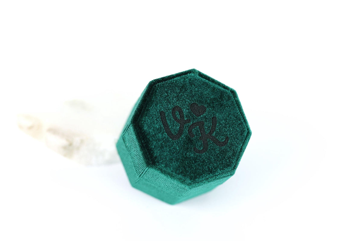 A green velvet ring box with a heart symbol on it.