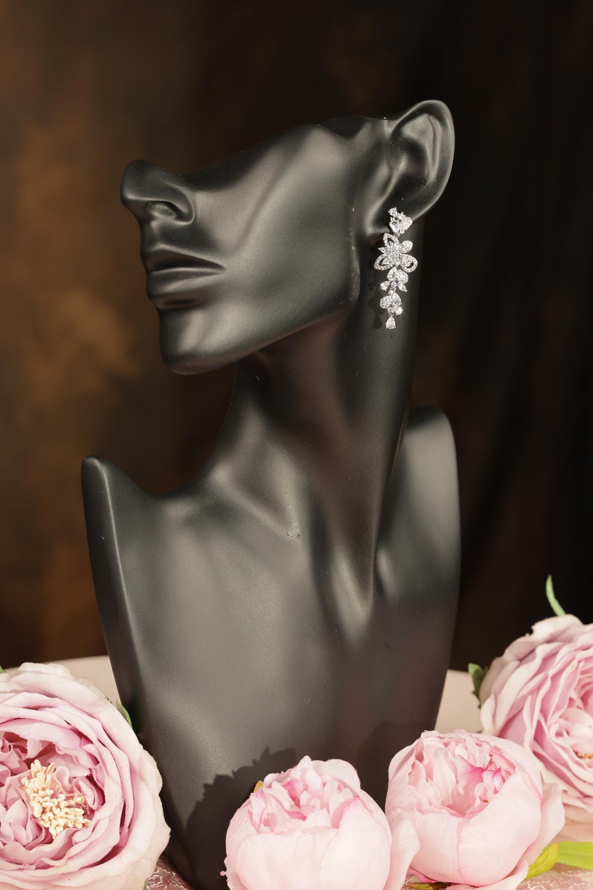 A black bust form with a floral earring on it, surrounded by pink peonies.
