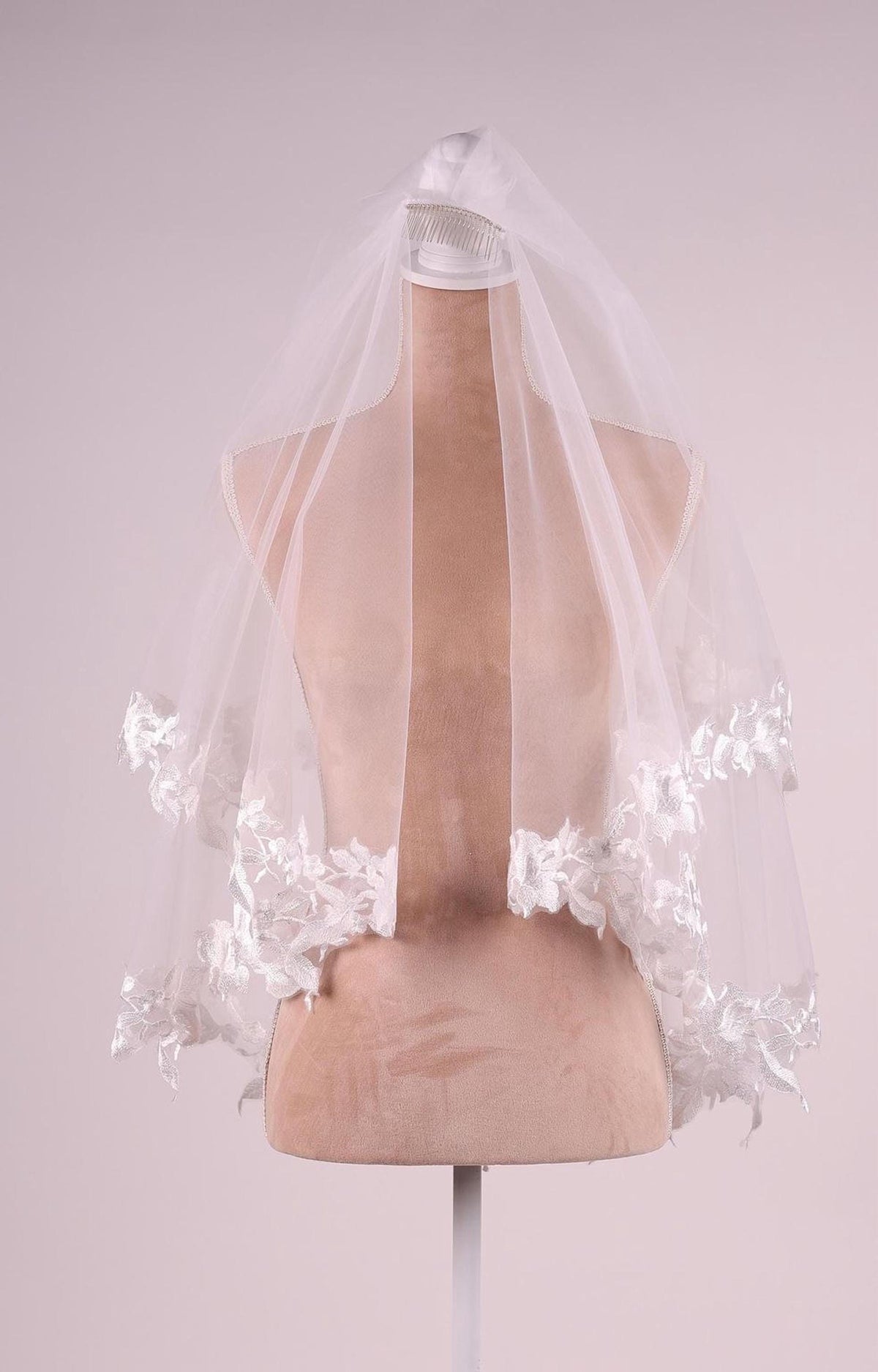 A mannequin wearing a white veil with delicate lace trim.