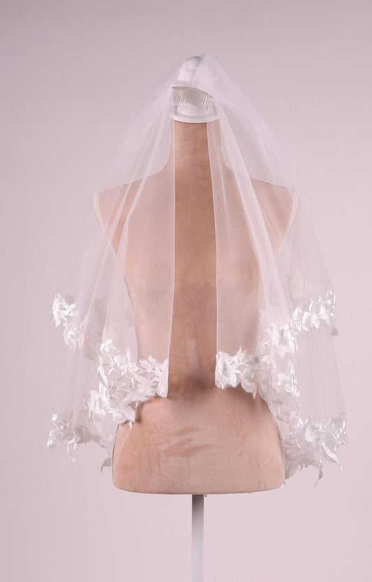 A mannequin wearing a white veil with delicate lace trim.