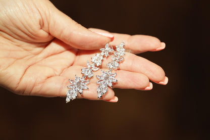 A close-up image of a person's hand holding a pair of elegant diamond earrings.