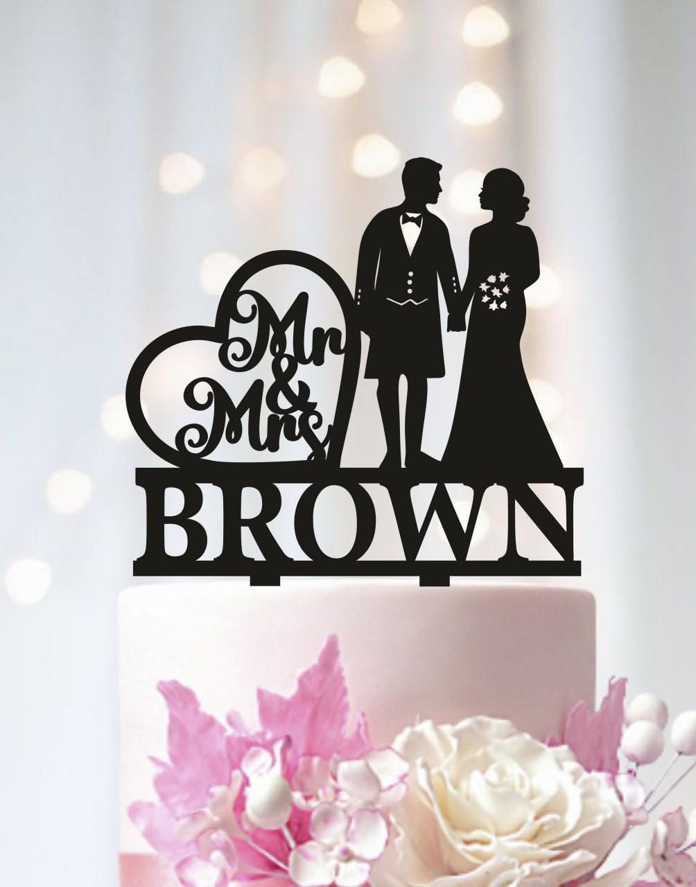 A black silhouette of a bride and groom on a wedding cake topper, with the text "Mr & Mrs Brown" below them.