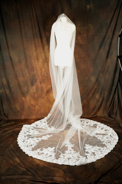 A white wedding dress with a long, flowing veil is displayed on a mannequin against a brown background.