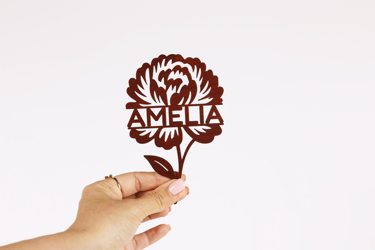 A hand holding a paper cutout of a flower with the name "Amalia" written on it.