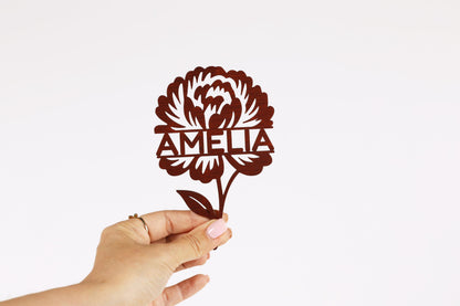 A hand holding a paper cutout of a flower with the name "Amalia" written on it.